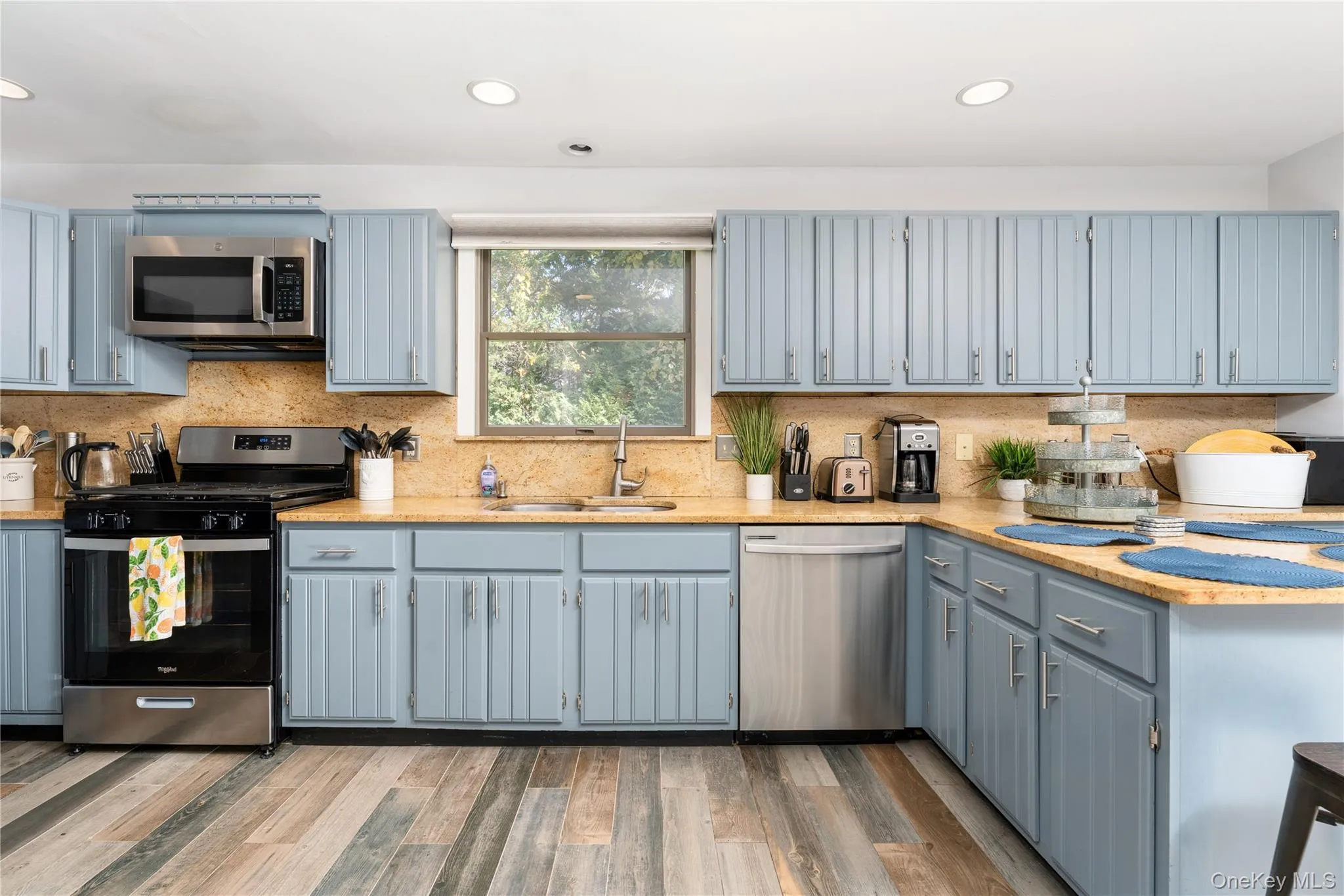 Kitchen with stainless steel appliances, decorative backsplash, light wood-style flooring, recessed lighting, and light stone countertops Kitchen with stainless steel appliances, decorative backsplash, light wood-style flooring, recessed lighting, and light stone countertops