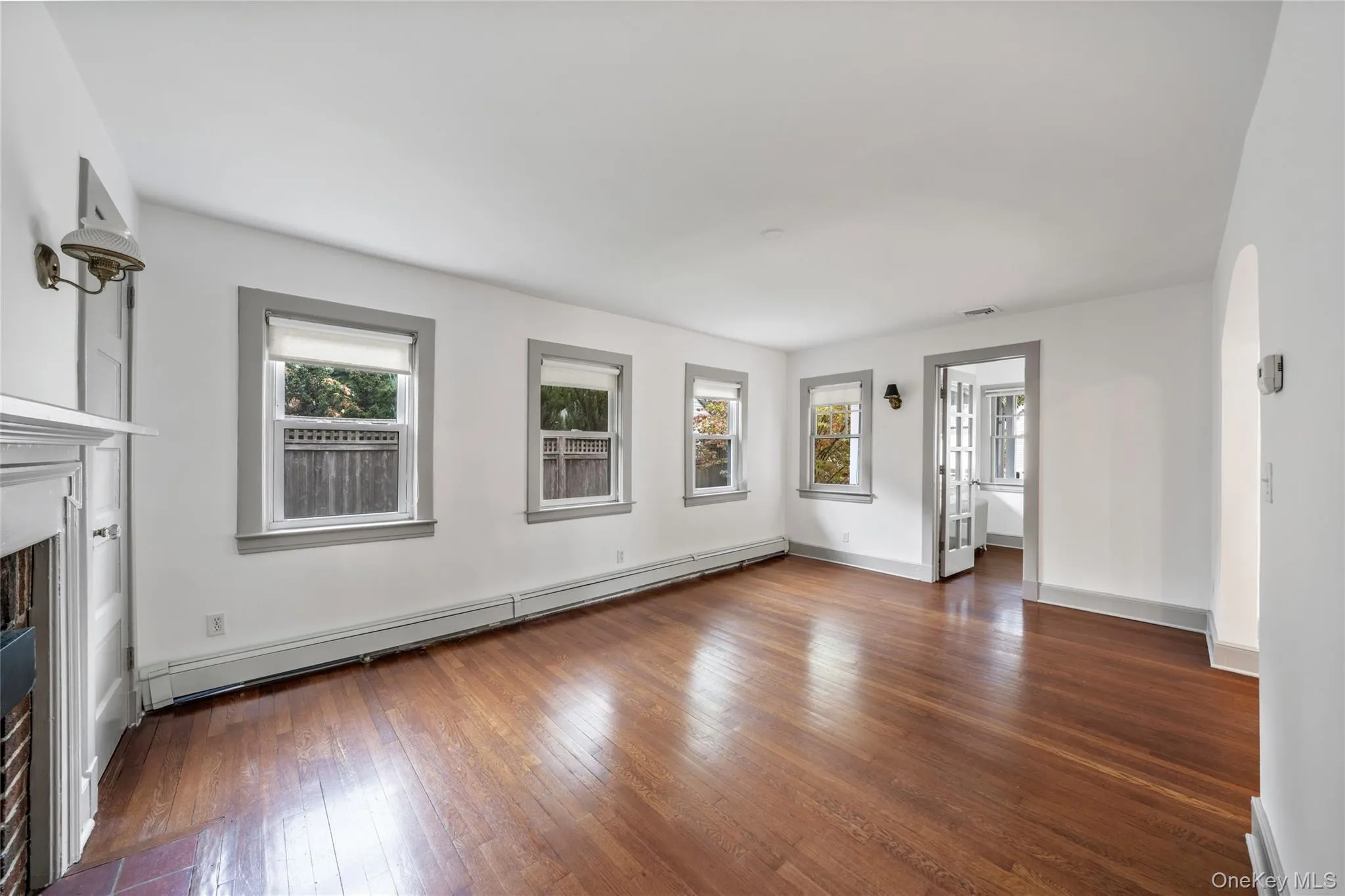 Unfurnished living room featuring a baseboard radiator, arched walkways, dark wood finished floors, and a fireplace Unfurnished living room featuring a baseboard radiator, arched walkways, dark wood finished floors, and a fireplace