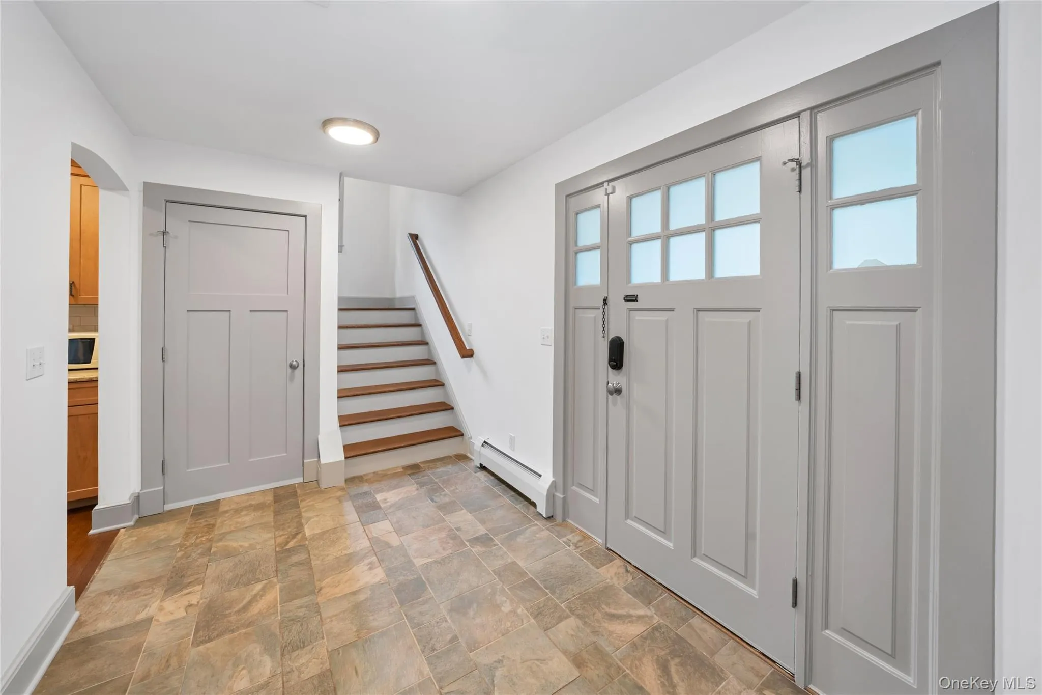 Foyer featuring baseboard heating, stone finish floors, stairway, and arched walkways Foyer featuring baseboard heating, stone finish floors, stairway, and arched walkways