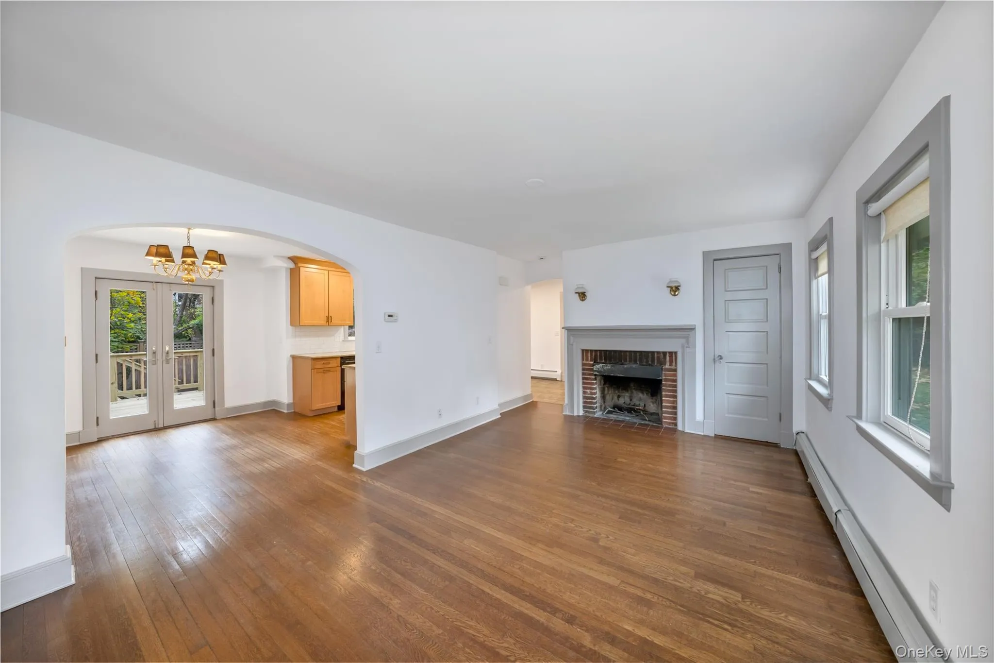 Unfurnished living room with healthy amount of natural light, a baseboard radiator, dark wood-type flooring, and a brick fireplace Unfurnished living room with healthy amount of natural light, a baseboard radiator, dark wood-type flooring, and a brick fireplace