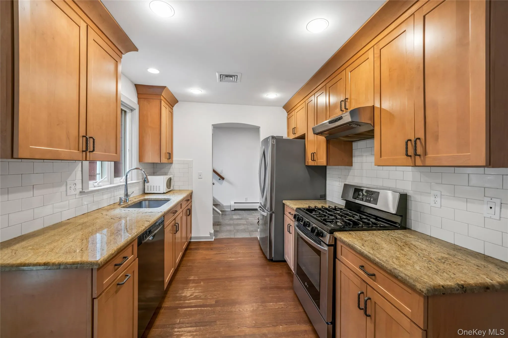 Kitchen featuring appliances with stainless steel finishes, light stone countertops, decorative backsplash, under cabinet range hood, and dark wood-style floors Kitchen featuring appliances with stainless steel finishes, light stone countertops, decorative backsplash, under cabinet range hood, and dark wood-style floors