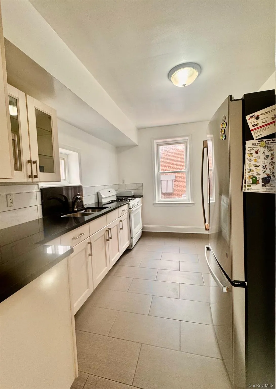 Kitchen with glass insert cabinets, freestanding refrigerator, white gas stove, white cabinetry, and light tile patterned floors Kitchen with glass insert cabinets, freestanding refrigerator, white gas stove, white cabinetry, and light tile patterned floors
