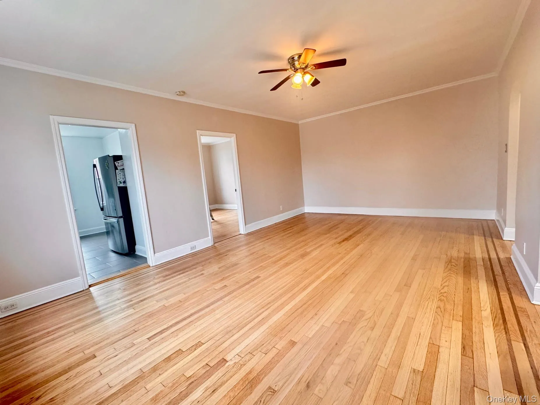 Empty room with crown molding, light wood-style flooring, and a ceiling fan Empty room with crown molding, light wood-style flooring, and a ceiling fan