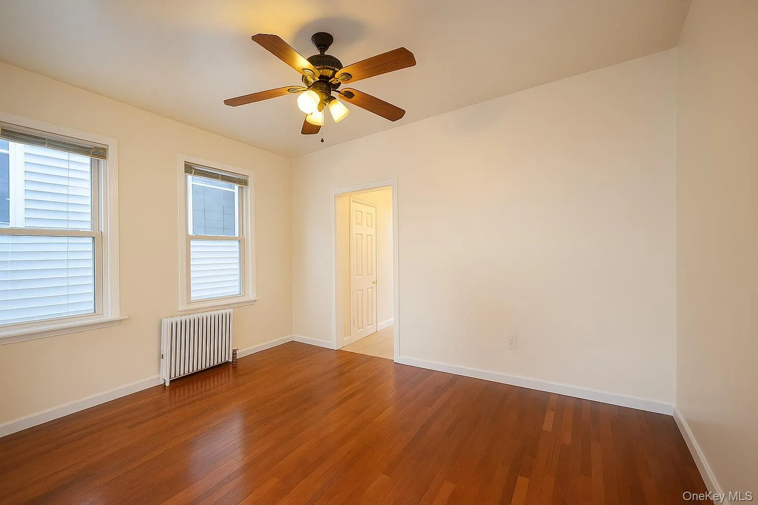 Spare room with radiator, wood finished floors, and ceiling fan Spare room with radiator, wood finished floors, and ceiling fan