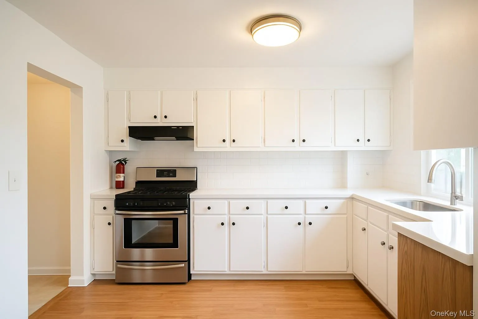 Kitchen with gas stove, tasteful backsplash, light wood-type flooring, and white cabinets Kitchen with gas stove, tasteful backsplash, light wood-type flooring, and white cabinets