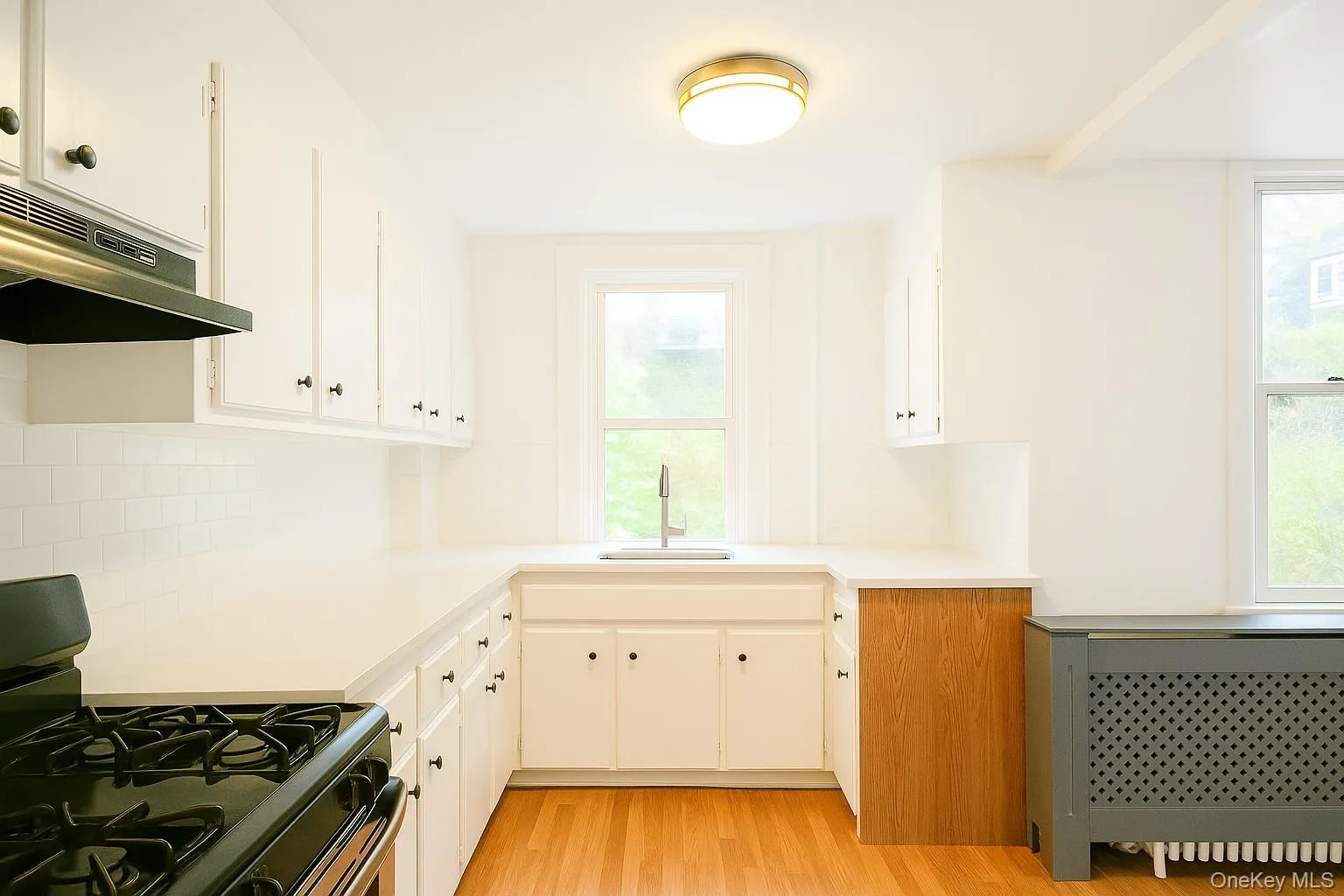 Kitchen featuring gas stove, radiator heating unit, light countertops, and white cabinetry Kitchen featuring gas stove, radiator heating unit, light countertops, and white cabinetry