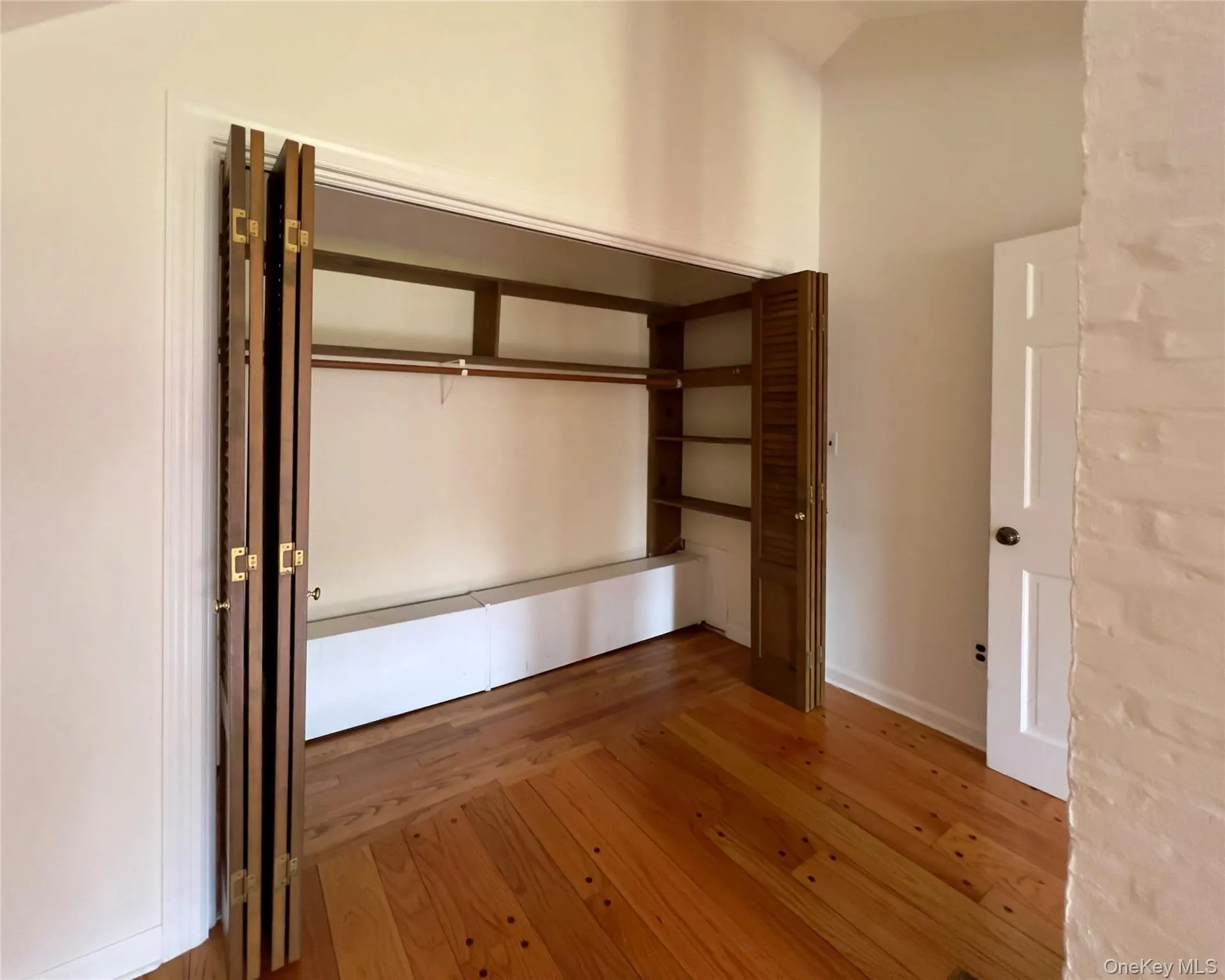 Large primary bedroom with hardwood floors, lofted ceiling, spacious closets and a baseboard heating unit Large primary bedroom with hardwood floors, lofted ceiling, spacious closets and a baseboard heating unit