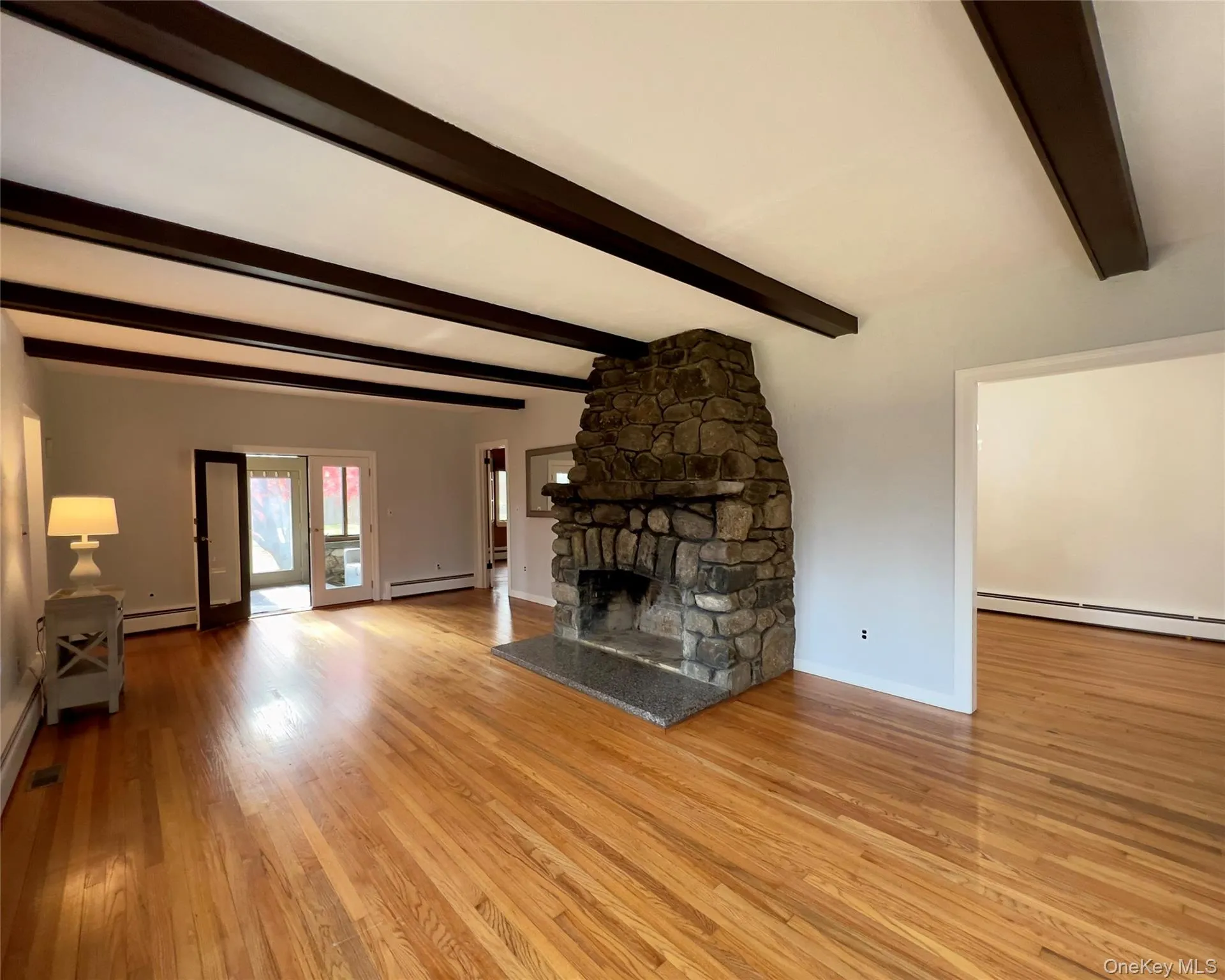 Unfurnished living room featuring a fireplace, hardwood floors, beam ceiling, and baseboard heating Unfurnished living room featuring a fireplace, hardwood floors, beam ceiling, and baseboard heating