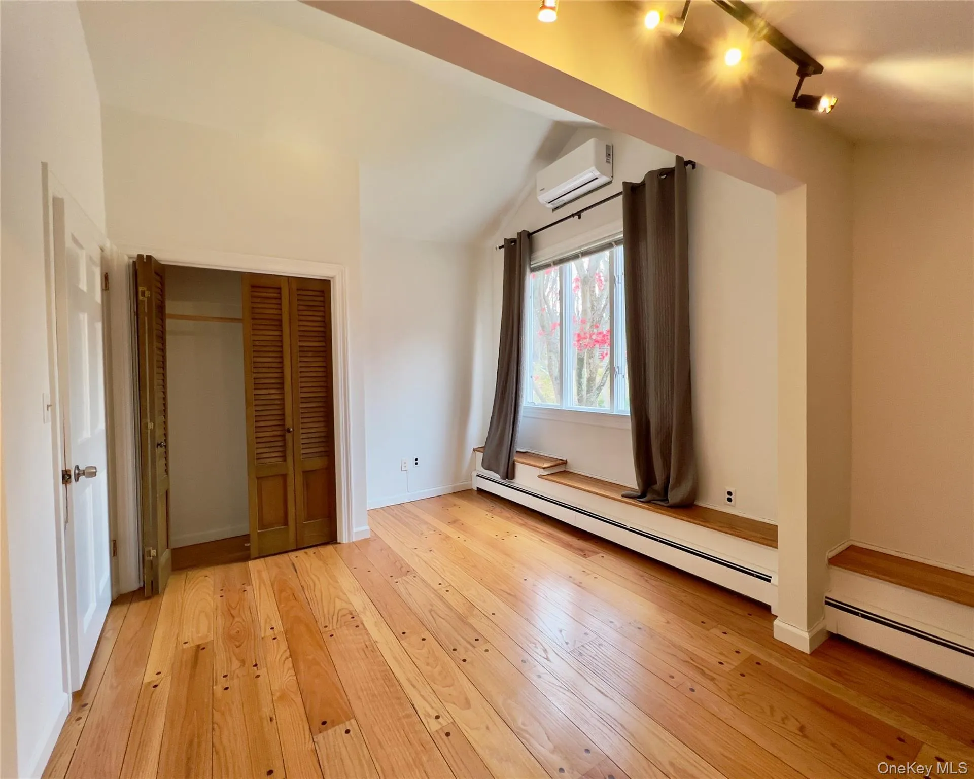 Bedroom #3, with lofted ceilings, baseboard heating, hardwood floors, a wall mounted AC, a closet, and track lighting Bedroom #3, with lofted ceilings, baseboard heating, hardwood floors, a wall mounted AC, a closet, and track lighting