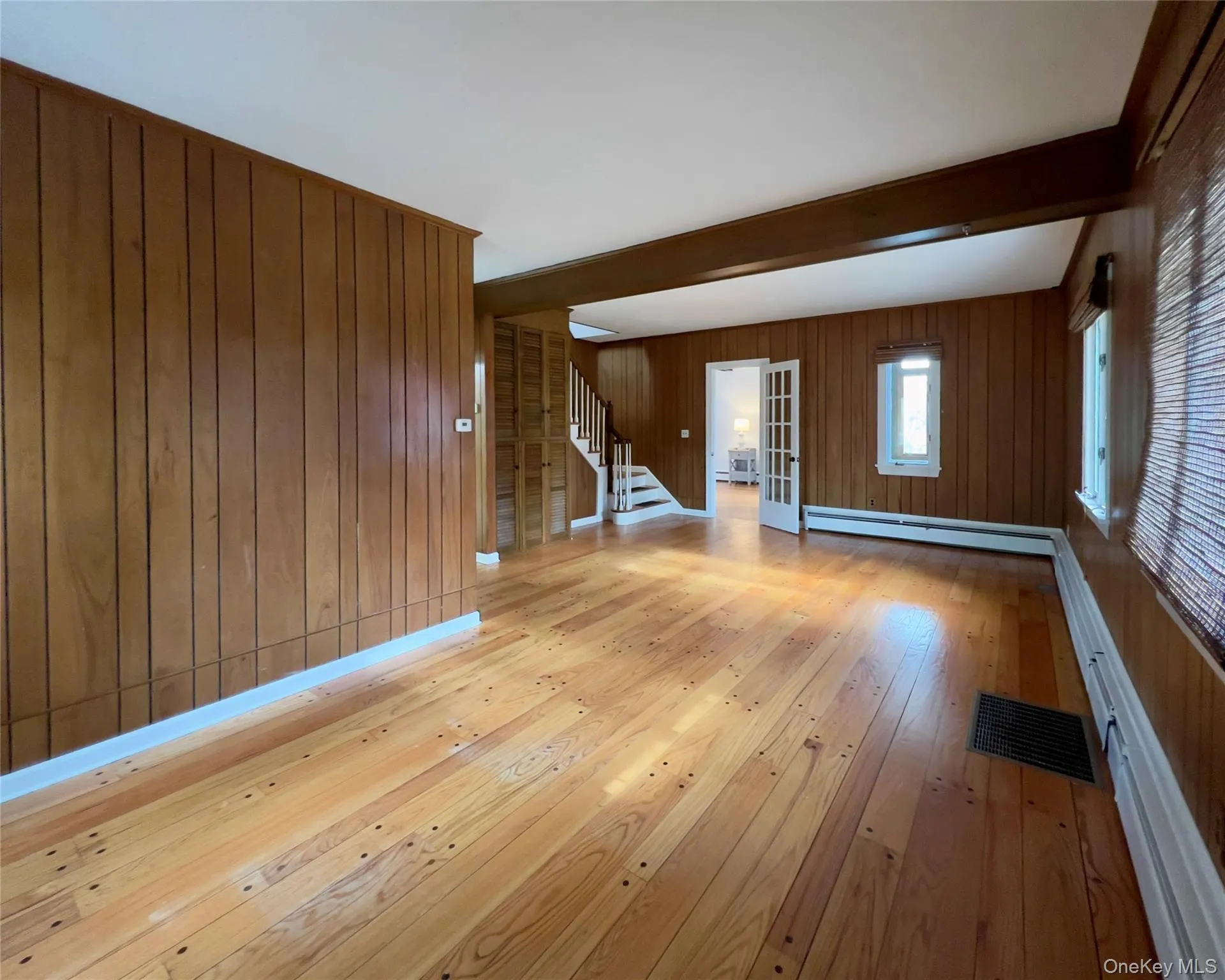 Living room featuring beam ceiling, baseboard heating, hardwood flooring, stairs, and wood walls Living room featuring beam ceiling, baseboard heating, hardwood flooring, stairs, and wood walls