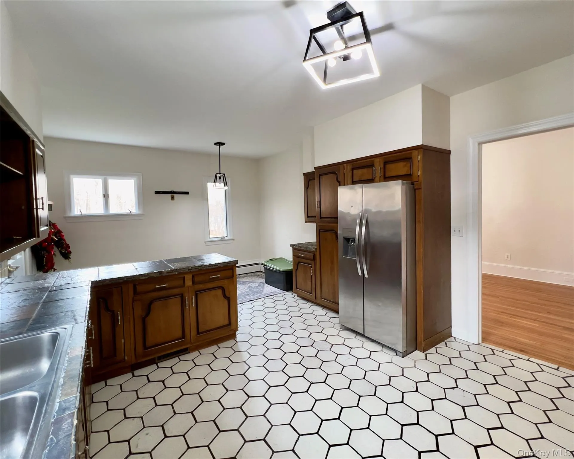 Kitchen with open shelves, stainless steel appliances, a peninsula, decorative backsplash, stone tile countertops, brown cabinetry and baseboard heating Kitchen with open shelves, stainless steel appliances, a peninsula, decorative backsplash, stone tile countertops, brown cabinetry and baseboard heating