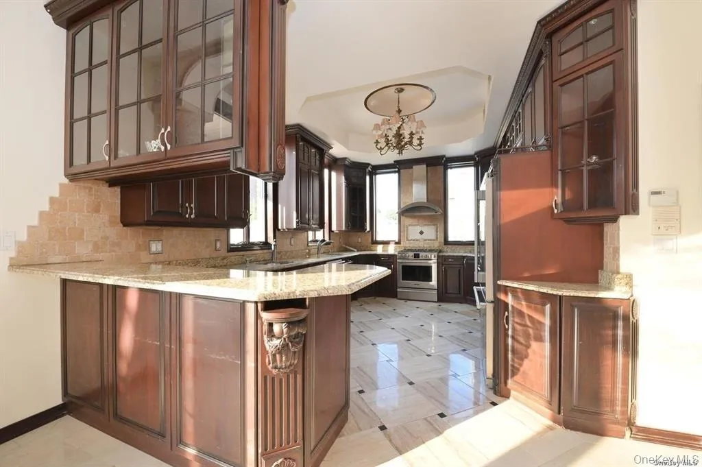 Kitchen featuring glass insert cabinets, dark brown cabinetry, tasteful backsplash, a peninsula, and light stone counters Kitchen featuring glass insert cabinets, dark brown cabinetry, tasteful backsplash, a peninsula, and light stone counters