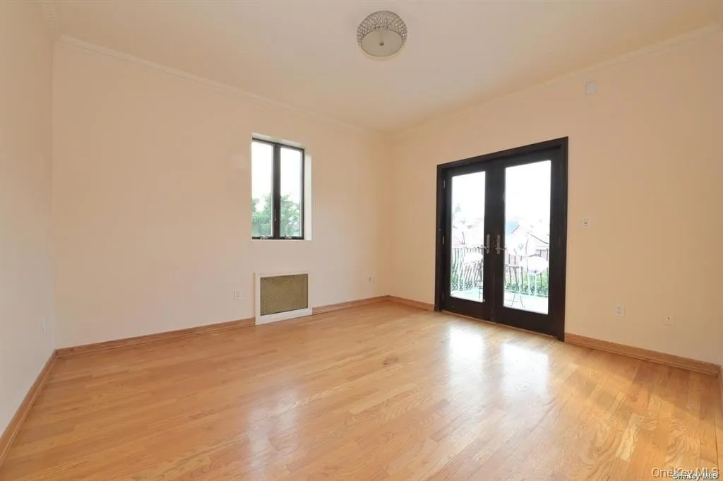 Empty room featuring crown molding, light wood-type flooring, french doors, and radiator heating unit Empty room featuring crown molding, light wood-type flooring, french doors, and radiator heating unit
