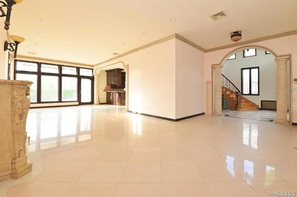 Empty room featuring crown molding, arched walkways, stairway, light tile patterned floors, and decorative columns Empty room featuring crown molding, arched walkways, stairway, light tile patterned floors, and decorative columns
