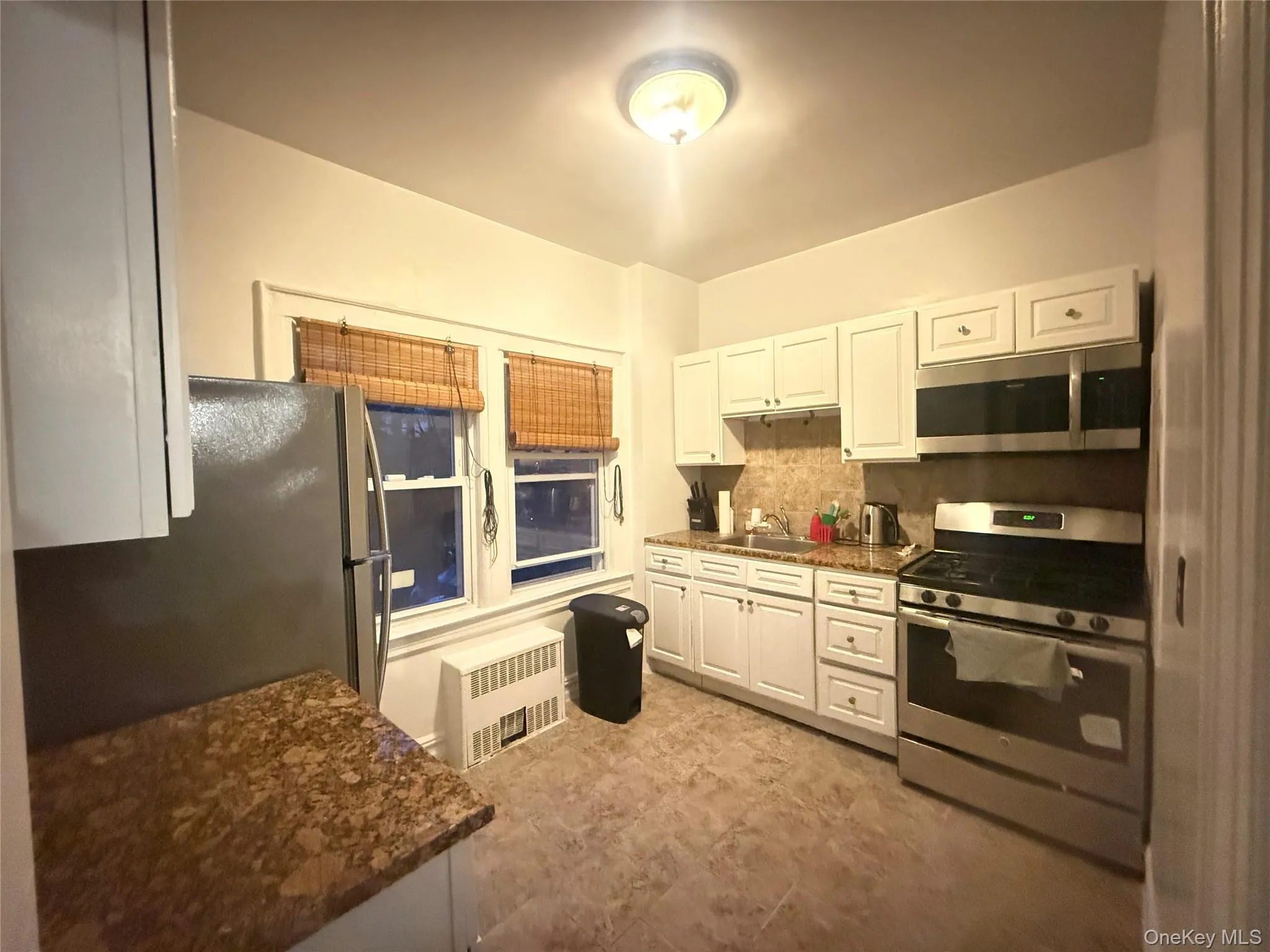 Kitchen featuring stainless steel appliances, decorative backsplash, dark stone counters, white cabinets, and radiator Kitchen featuring stainless steel appliances, decorative backsplash, dark stone counters, white cabinets, and radiator