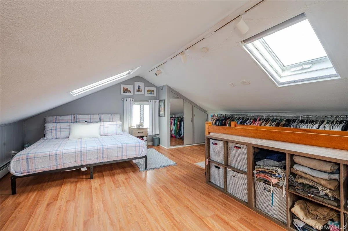 Bedroom featuring a skylight, track lighting, lofted ceiling, light wood finished floors, and a textured ceiling Bedroom featuring a skylight, track lighting, lofted ceiling, light wood finished floors, and a textured ceiling
