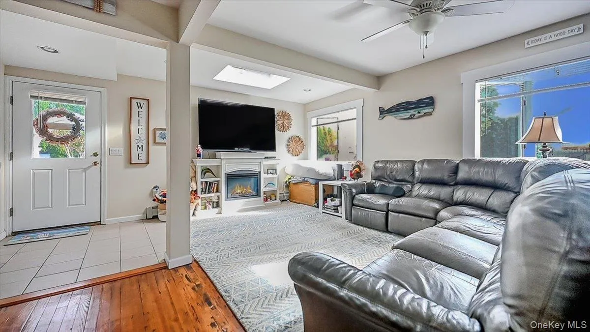 Living area featuring a skylight, light wood finished floors, a glass covered fireplace, and ceiling fan Living area featuring a skylight, light wood finished floors, a glass covered fireplace, and ceiling fan