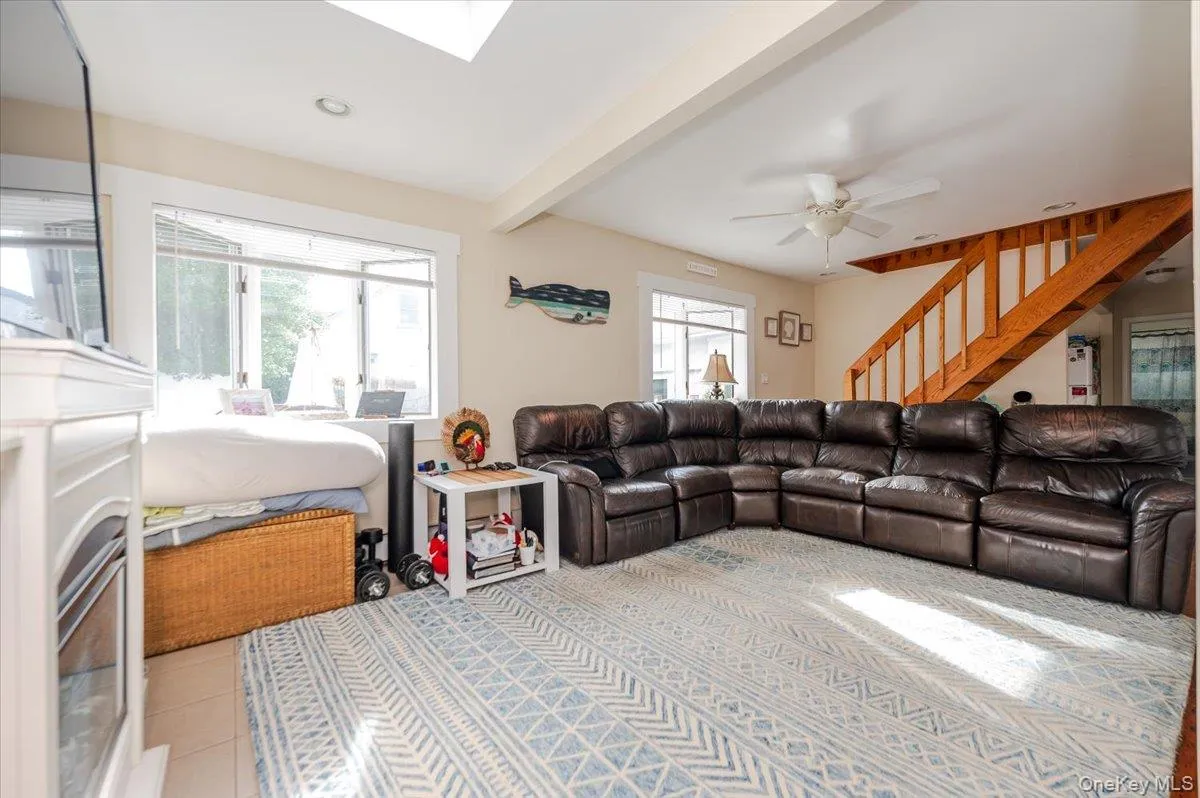 Living area featuring beamed ceiling, light tile patterned flooring, stairs, and a skylight Living area featuring beamed ceiling, light tile patterned flooring, stairs, and a skylight