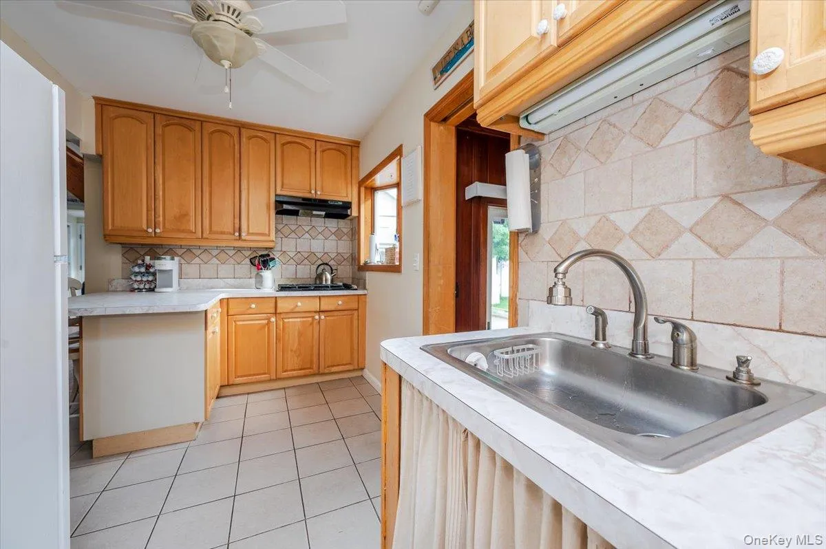 Kitchen featuring light countertops, decorative backsplash, light tile patterned floors, freestanding refrigerator, and a ceiling fan Kitchen featuring light countertops, decorative backsplash, light tile patterned floors, freestanding refrigerator, and a ceiling fan