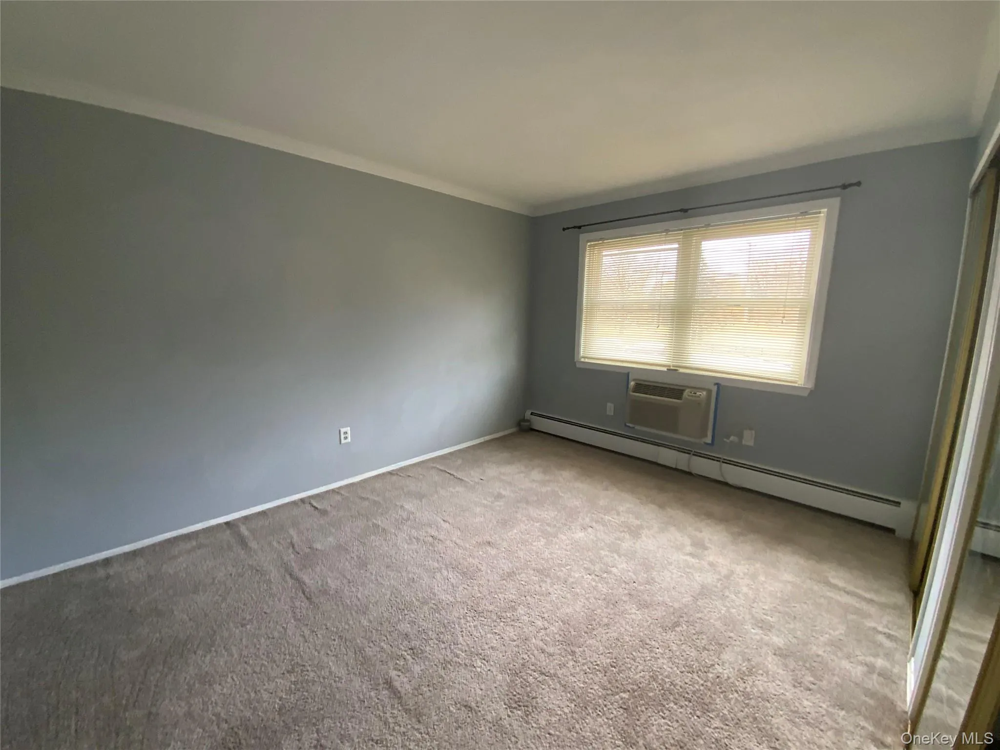 Carpeted empty room with a baseboard heating unit, an AC wall unit, and ornamental molding Carpeted empty room with a baseboard heating unit, an AC wall unit, and ornamental molding