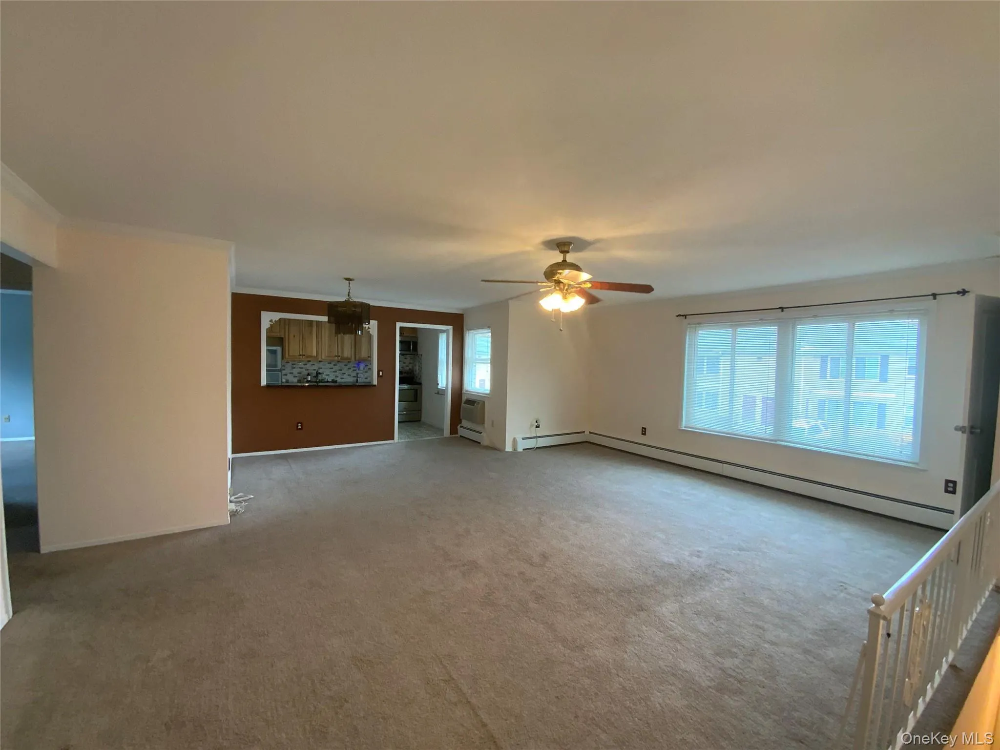 Unfurnished living room featuring healthy amount of natural light, carpet floors, baseboard heating, and ornamental molding Unfurnished living room featuring healthy amount of natural light, carpet floors, baseboard heating, and ornamental molding
