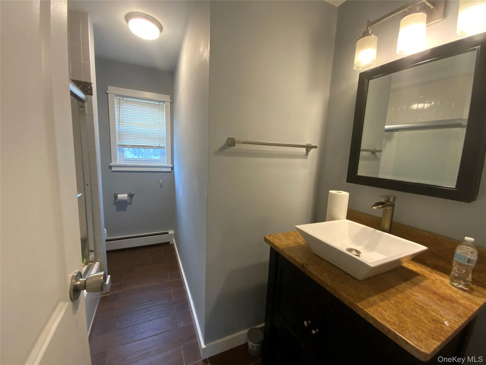 Bathroom featuring vanity, baseboard heating, dark wood-style flooring, and a shower with door Bathroom featuring vanity, baseboard heating, dark wood-style flooring, and a shower with door