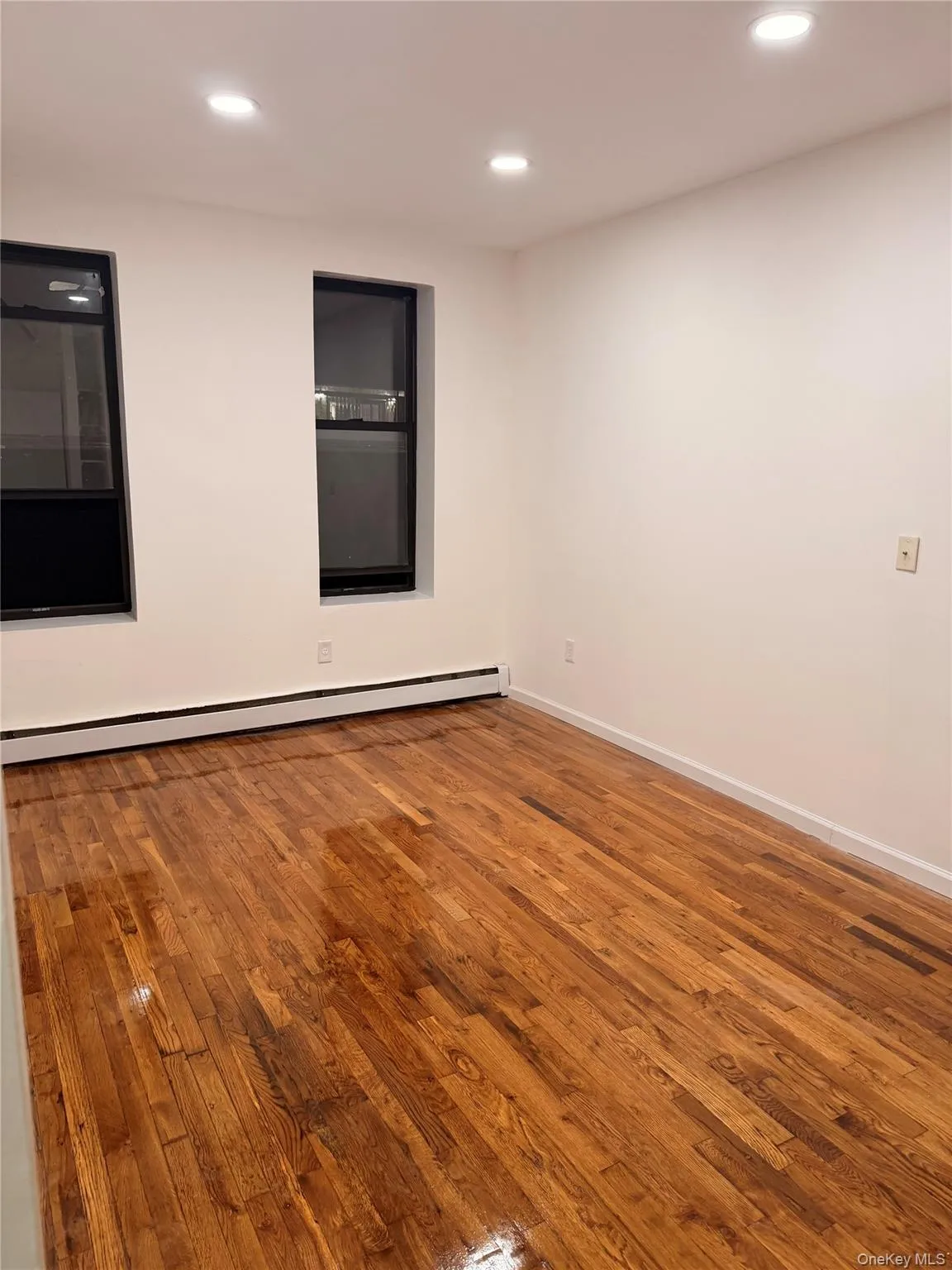Empty room featuring wood finished floors, a baseboard radiator, and recessed lighting Empty room featuring wood finished floors, a baseboard radiator, and recessed lighting