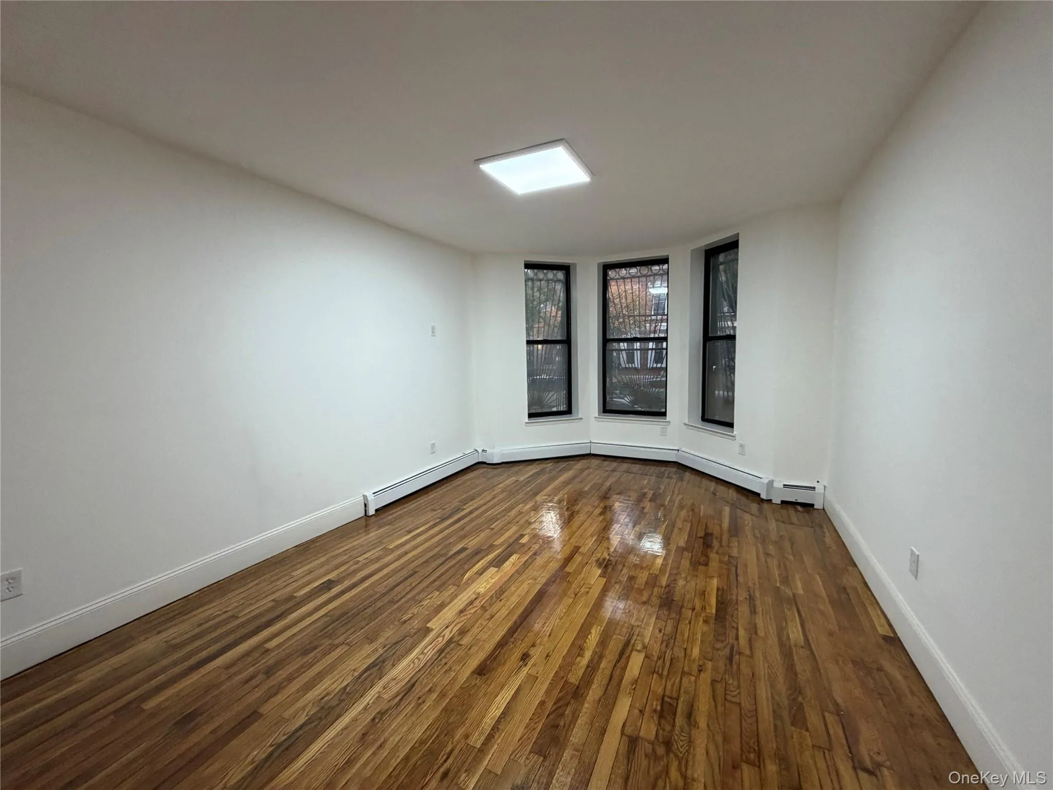 Unfurnished room featuring dark wood-style floors and a baseboard radiator Unfurnished room featuring dark wood-style floors and a baseboard radiator