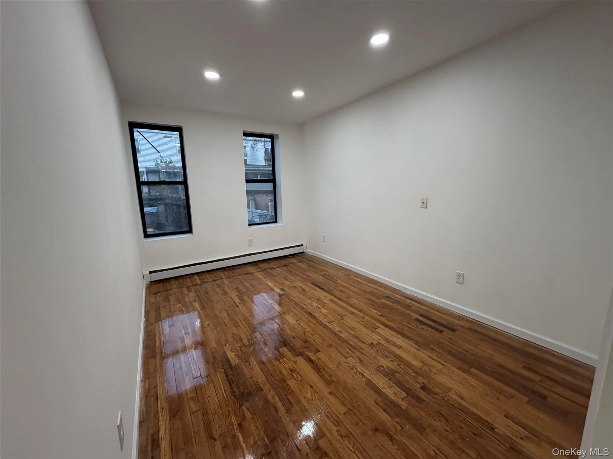 Empty room featuring dark wood finished floors, recessed lighting, and a baseboard heating unit Empty room featuring dark wood finished floors, recessed lighting, and a baseboard heating unit