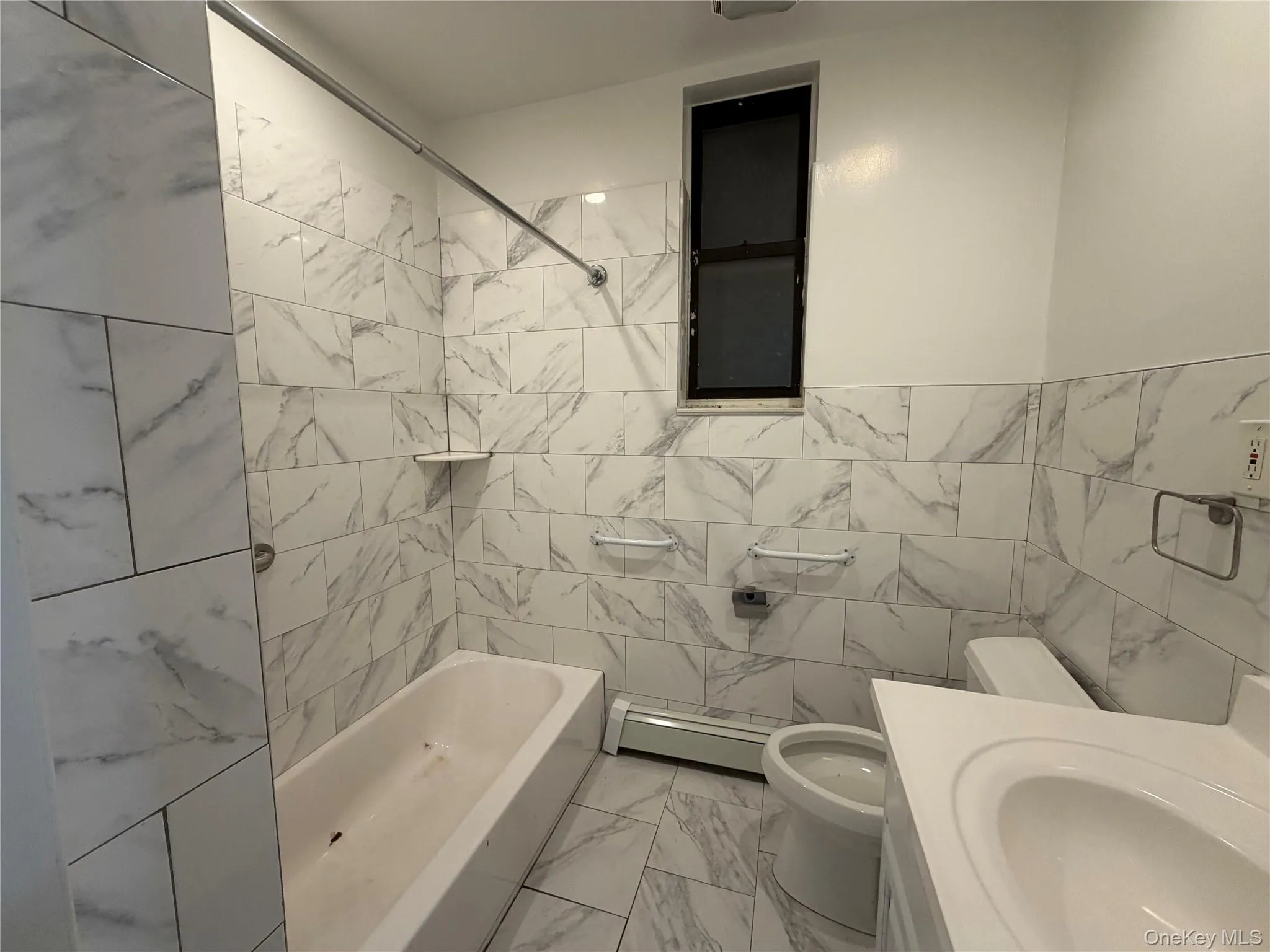 Full bath featuring tile walls, light marble finish flooring, baseboard heating, vanity, and shower / tub combination Full bath featuring tile walls, light marble finish flooring, baseboard heating, vanity, and shower / tub combination