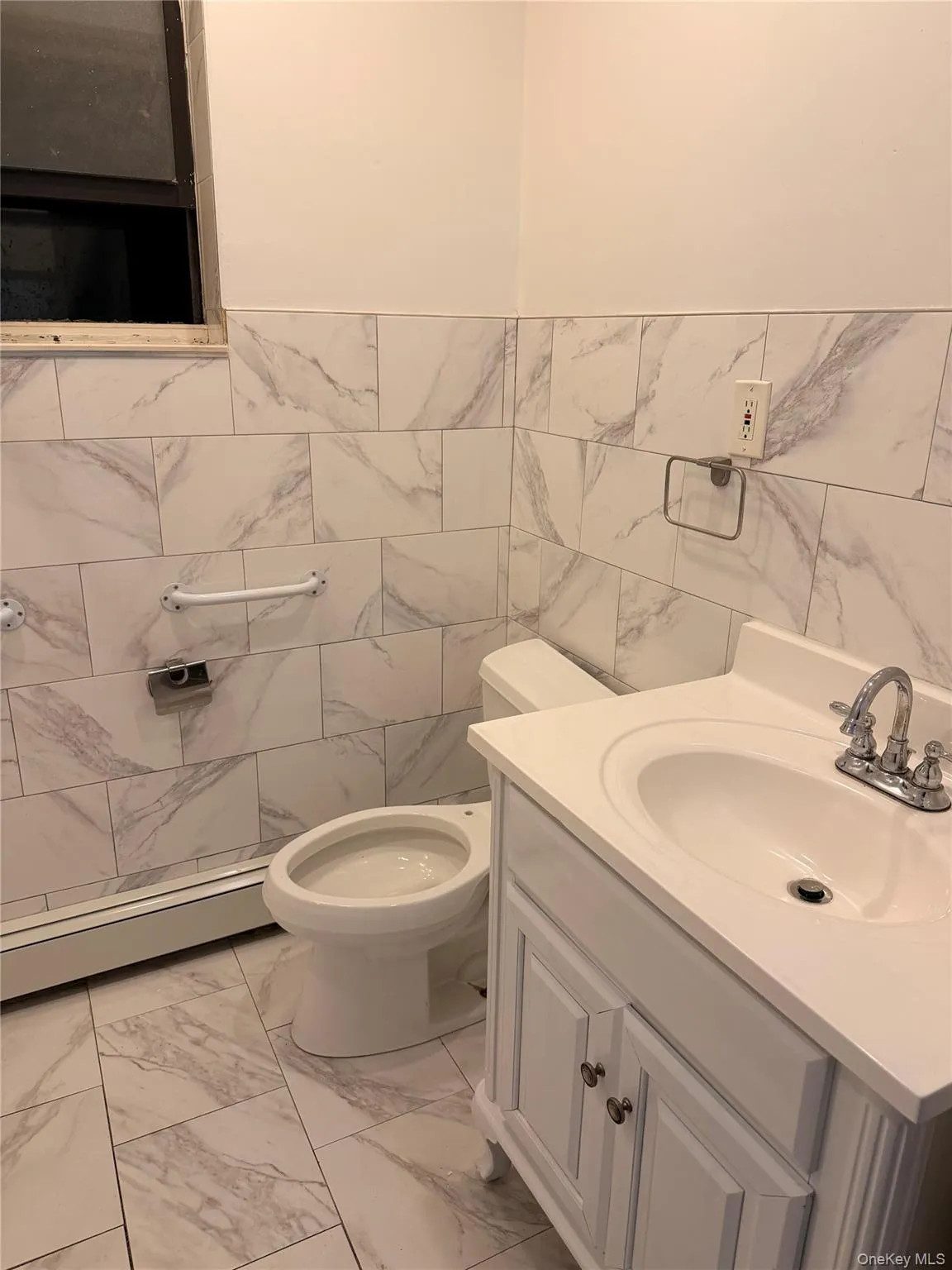 Bathroom featuring a baseboard heating unit, light marble finish flooring, tile walls, and vanity Bathroom featuring a baseboard heating unit, light marble finish flooring, tile walls, and vanity