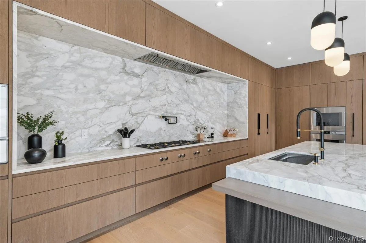 Kitchen with light stone countertops, hanging light fixtures, light wood-style flooring, backsplash, and brown cabinets