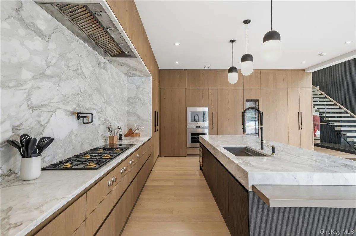 Kitchen with modern cabinets, light stone counters, decorative light fixtures, appliances with stainless steel finishes, and wall chimney exhaust hood