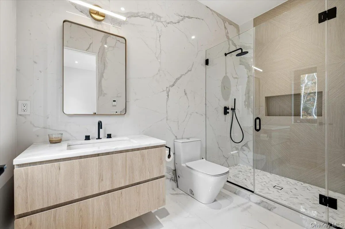 Full bath featuring stone wall, a marble finish shower, vanity, and light marble finish floors
