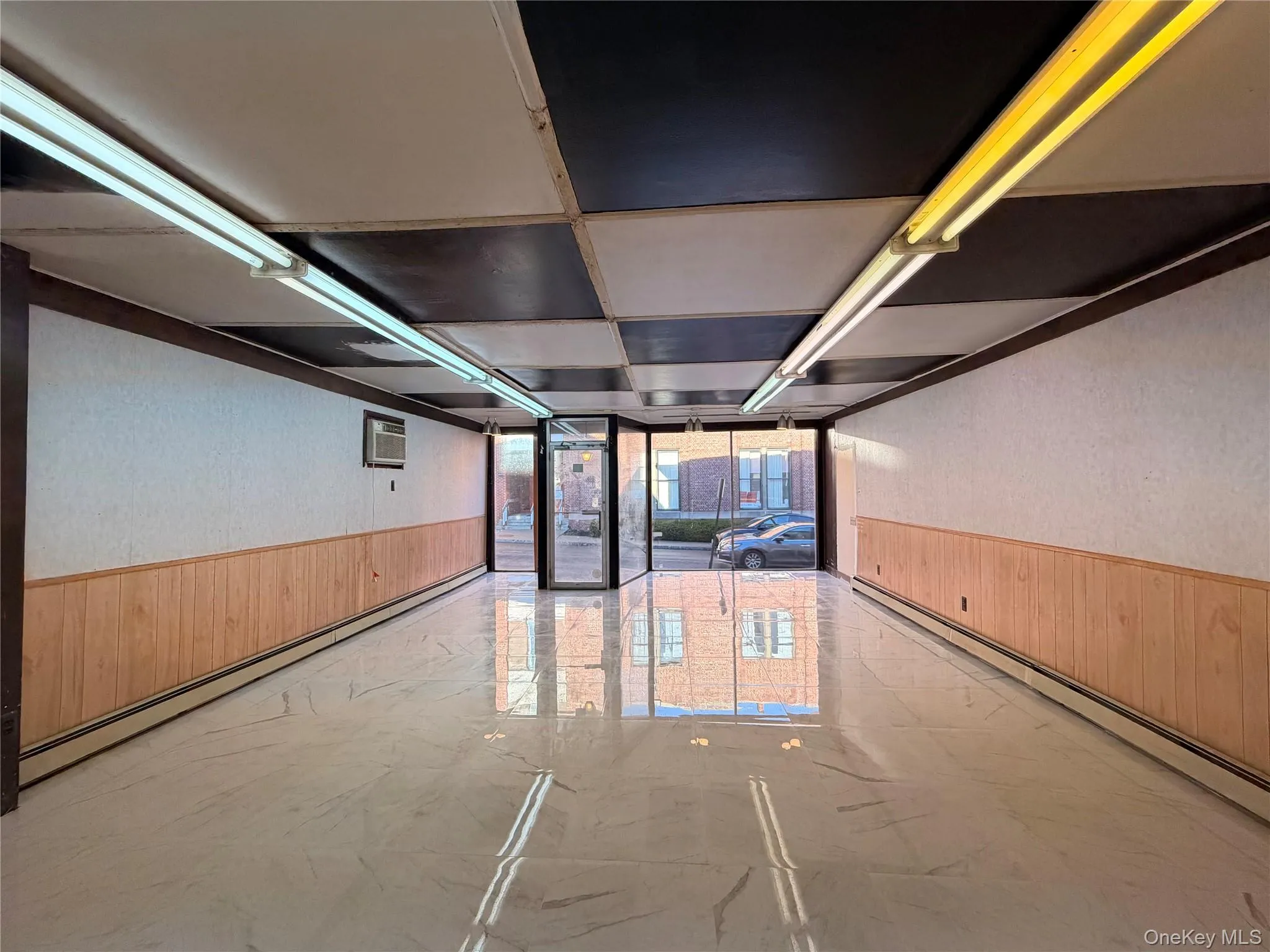Empty room with a wainscoted wall, wooden walls, a baseboard radiator, light marble finish flooring, and a wall unit AC Empty room with a wainscoted wall, wooden walls, a baseboard radiator, light marble finish flooring, and a wall unit AC