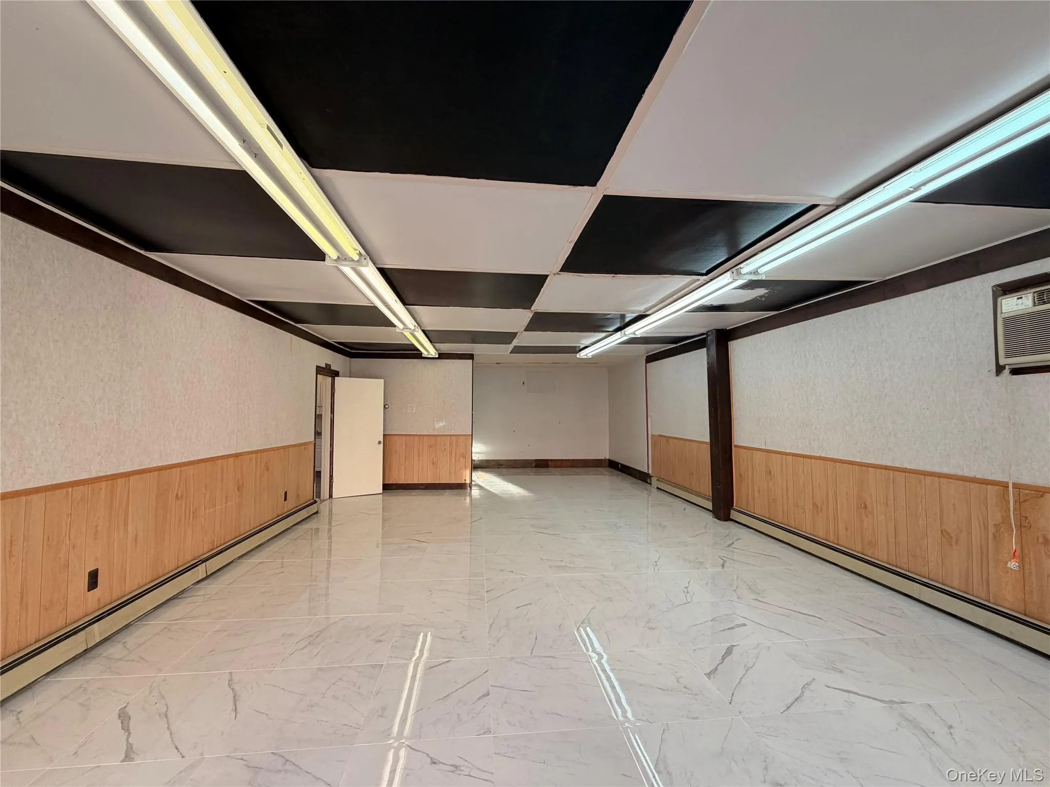Empty room featuring wainscoting, light marble finish flooring, a baseboard radiator, wallpapered walls, and wooden walls Empty room featuring wainscoting, light marble finish flooring, a baseboard radiator, wallpapered walls, and wooden walls