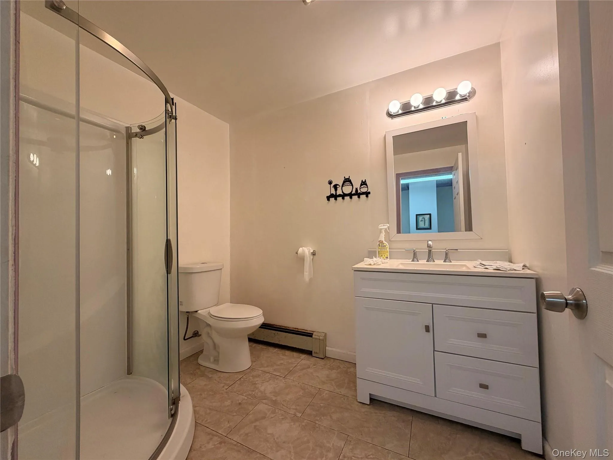 Full bathroom featuring a baseboard radiator, a shower stall, vanity, and light tile patterned floors Full bathroom featuring a baseboard radiator, a shower stall, vanity, and light tile patterned floors