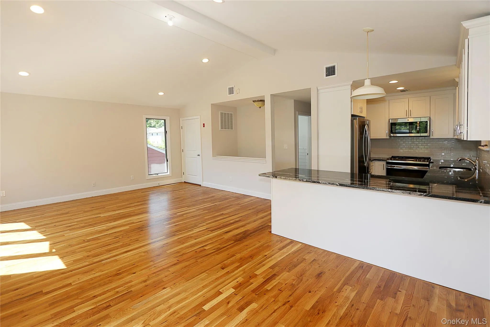 Kitchen with dark stone countertops, recessed lighting, light wood-type flooring, stainless steel appliances, and hanging light fixtures Kitchen with dark stone countertops, recessed lighting, light wood-type flooring, stainless steel appliances, and hanging light fixtures