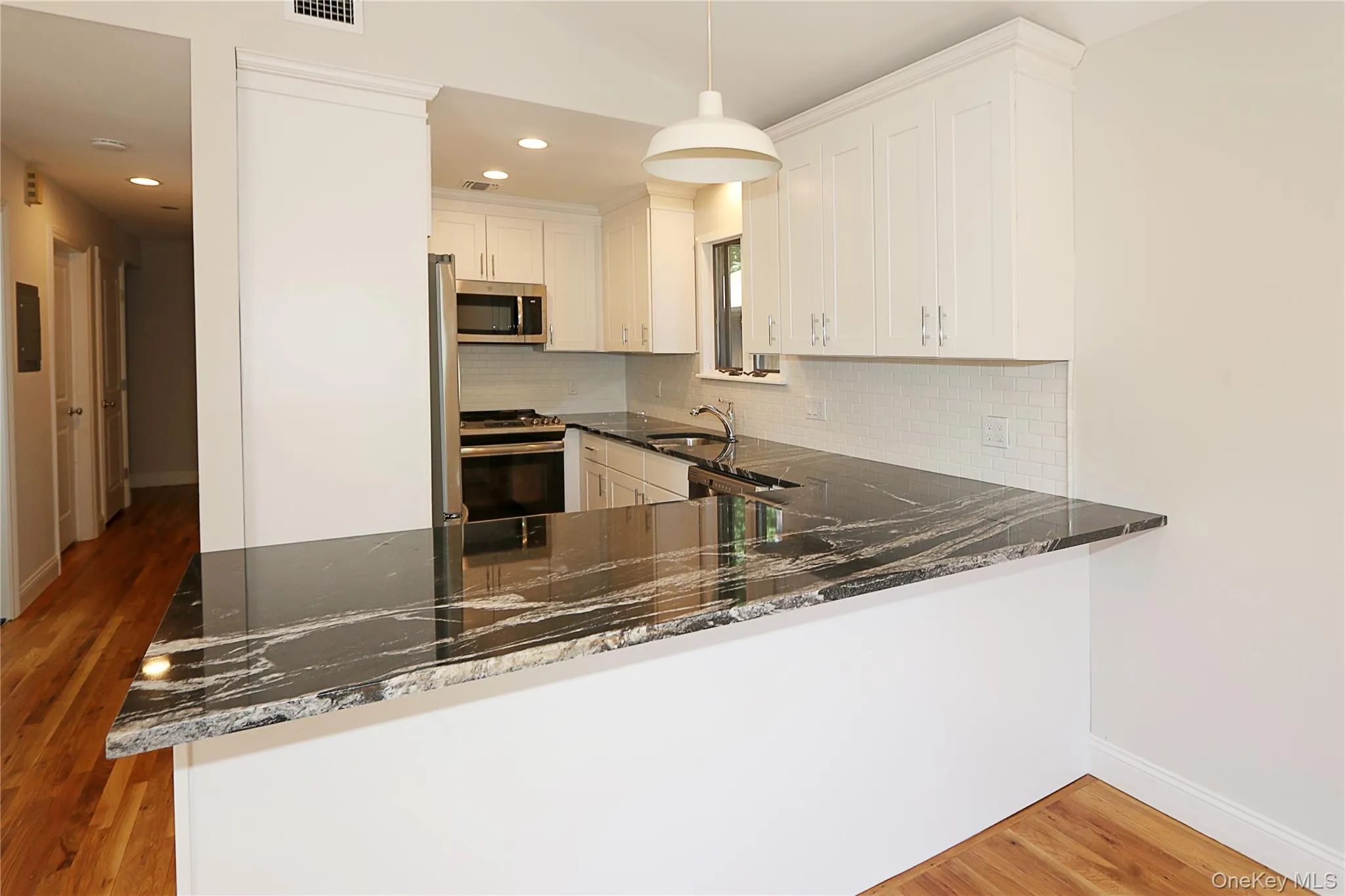 Kitchen with backsplash, light wood-style floors, dark stone countertops, appliances with stainless steel finishes, and pendant lighting Kitchen with backsplash, light wood-style floors, dark stone countertops, appliances with stainless steel finishes, and pendant lighting
