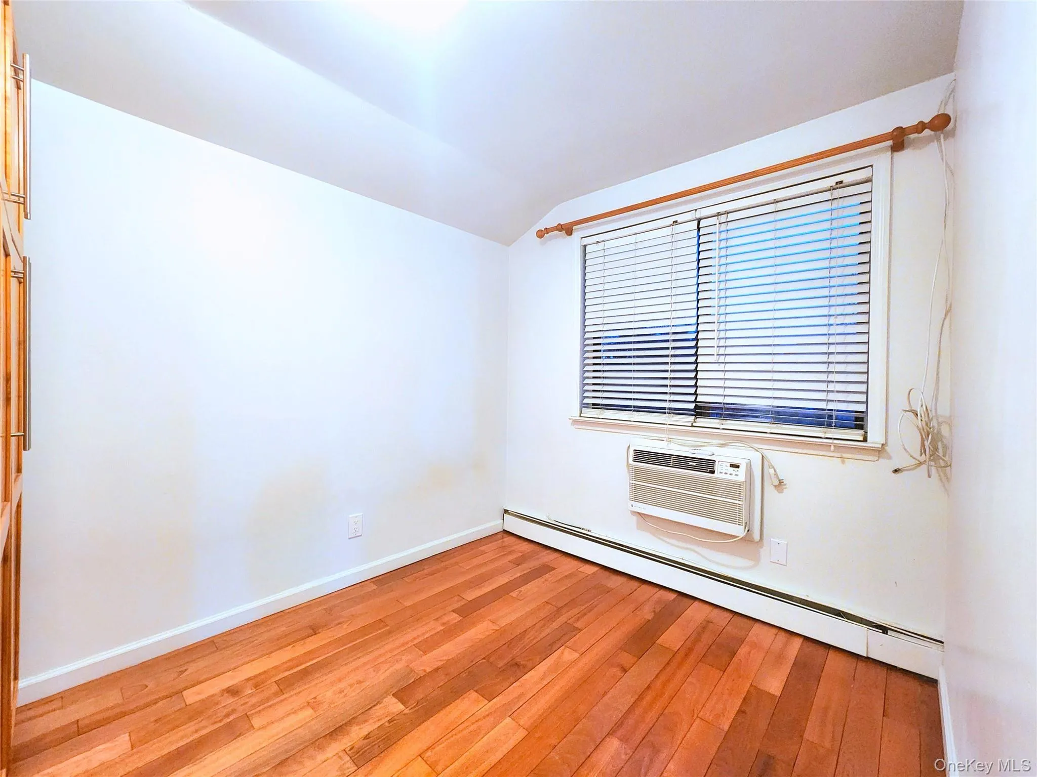 Spare room featuring baseboard heating, vaulted ceiling, light wood-style flooring, and an AC wall unit Spare room featuring baseboard heating, vaulted ceiling, light wood-style flooring, and an AC wall unit