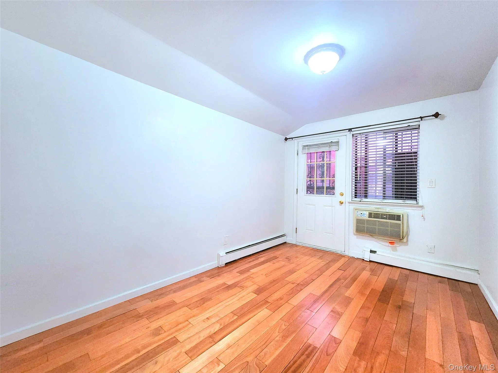 Spare room featuring baseboard heating, lofted ceiling, and light wood finished floors Spare room featuring baseboard heating, lofted ceiling, and light wood finished floors