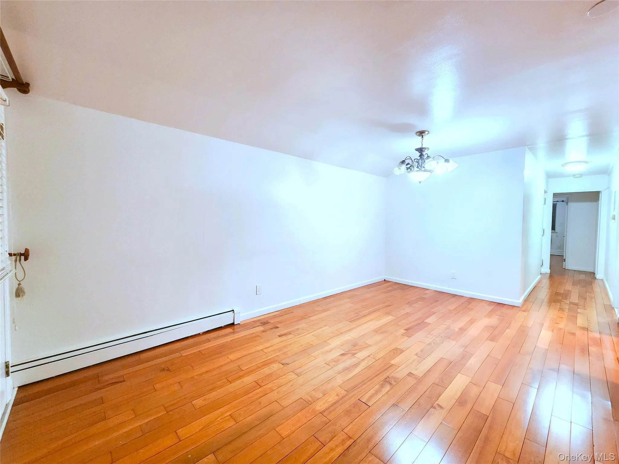 Unfurnished room featuring a chandelier, a baseboard heating unit, and light wood-style floors Unfurnished room featuring a chandelier, a baseboard heating unit, and light wood-style floors