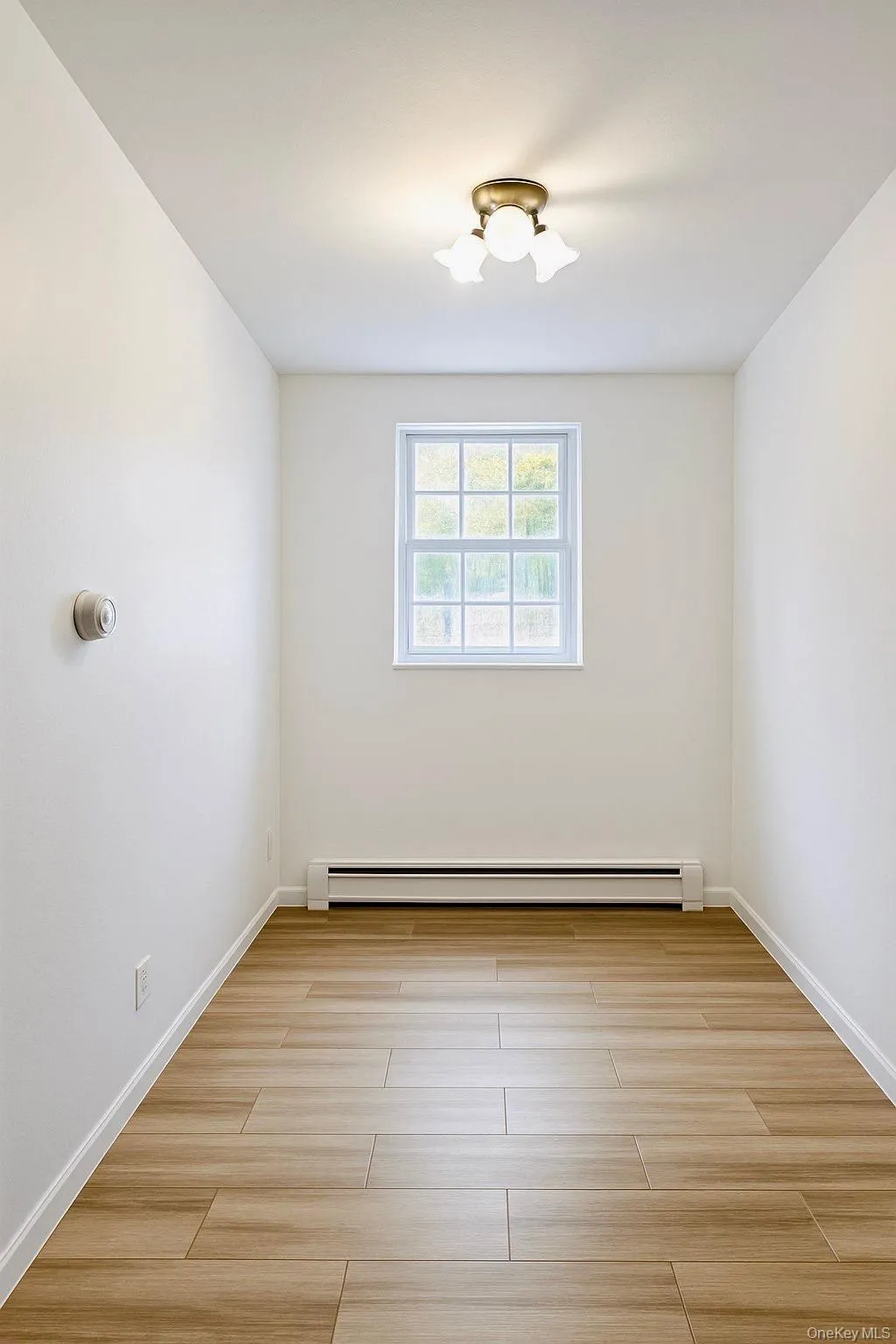 Unfurnished room featuring light wood finished floors and baseboard heating Unfurnished room featuring light wood finished floors and baseboard heating