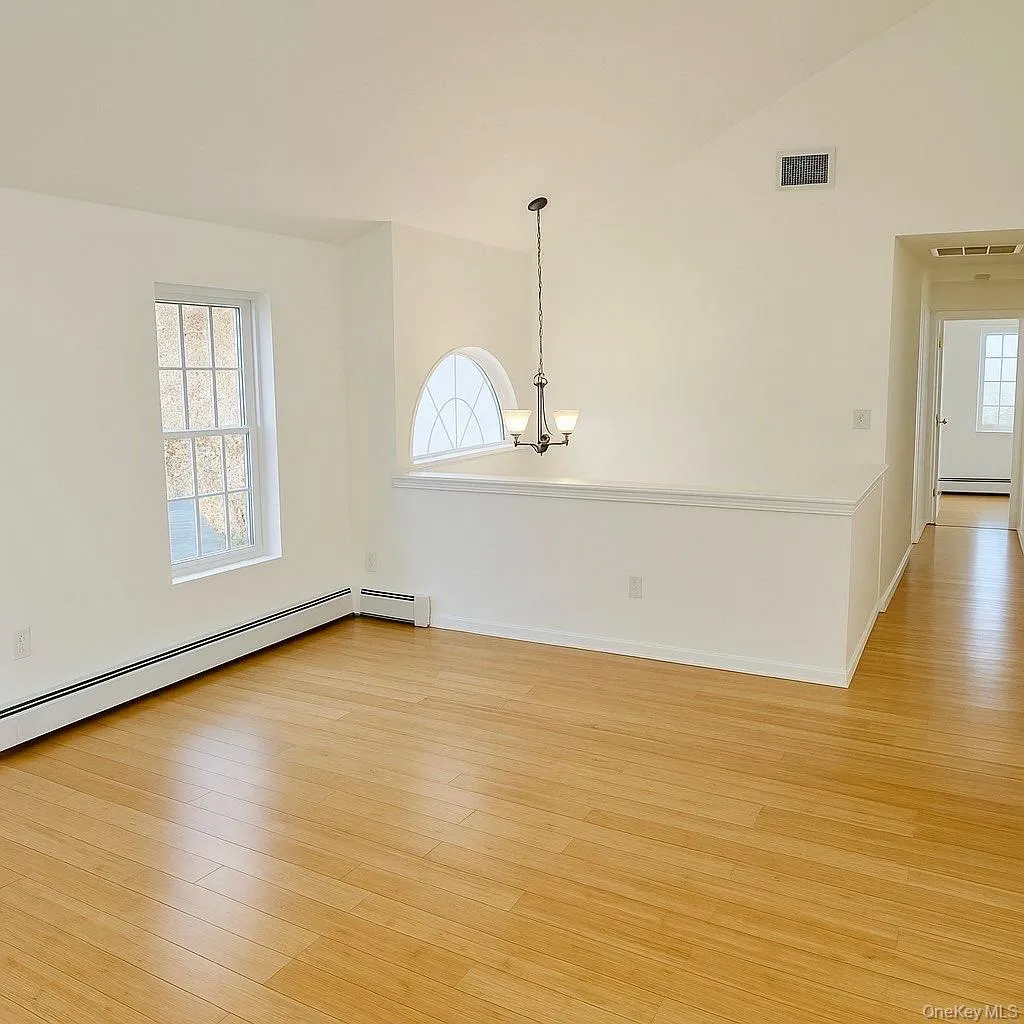Spare room featuring vaulted ceiling, light wood-type flooring, and a chandelier Spare room featuring vaulted ceiling, light wood-type flooring, and a chandelier