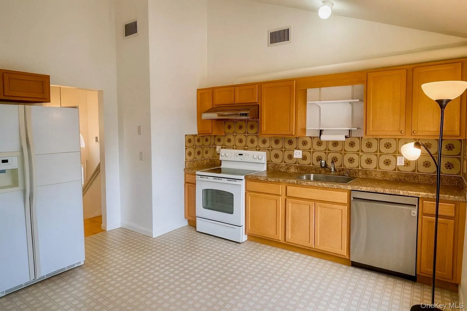 Kitchen featuring light floors, white appliances, under cabinet range hood, tasteful backsplash, and brown cabinetry Kitchen featuring light floors, white appliances, under cabinet range hood, tasteful backsplash, and brown cabinetry