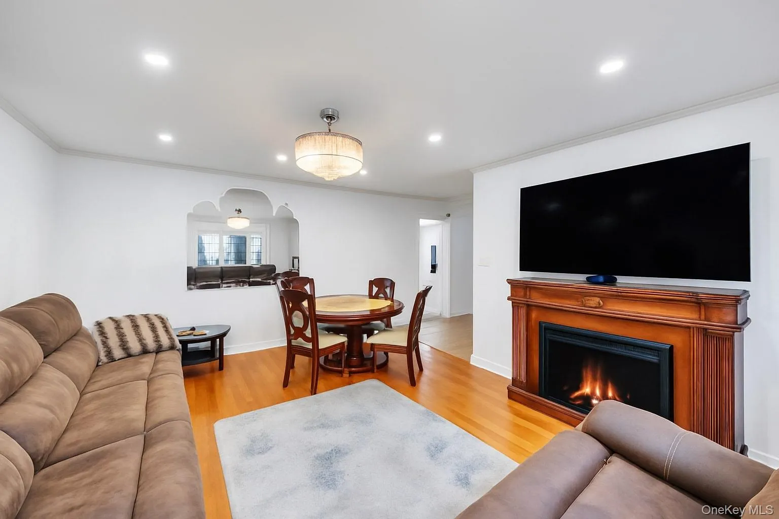 Living area featuring crown molding, arched walkways, light wood-type flooring, a lit fireplace, and recessed lighting Living area featuring crown molding, arched walkways, light wood-type flooring, a lit fireplace, and recessed lighting