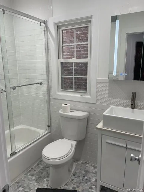 Bathroom with vanity, shower / bath combination with glass door, and tile walls Bathroom with vanity, shower / bath combination with glass door, and tile walls