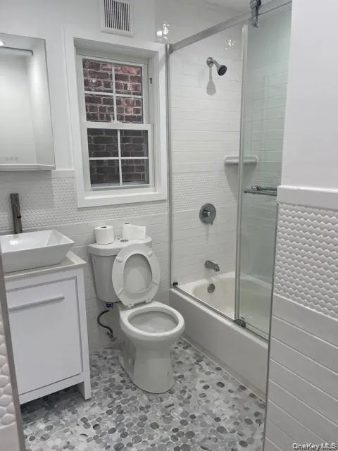 Full bath featuring tile walls, combined bath / shower with glass door, wainscoting, and vanity Full bath featuring tile walls, combined bath / shower with glass door, wainscoting, and vanity