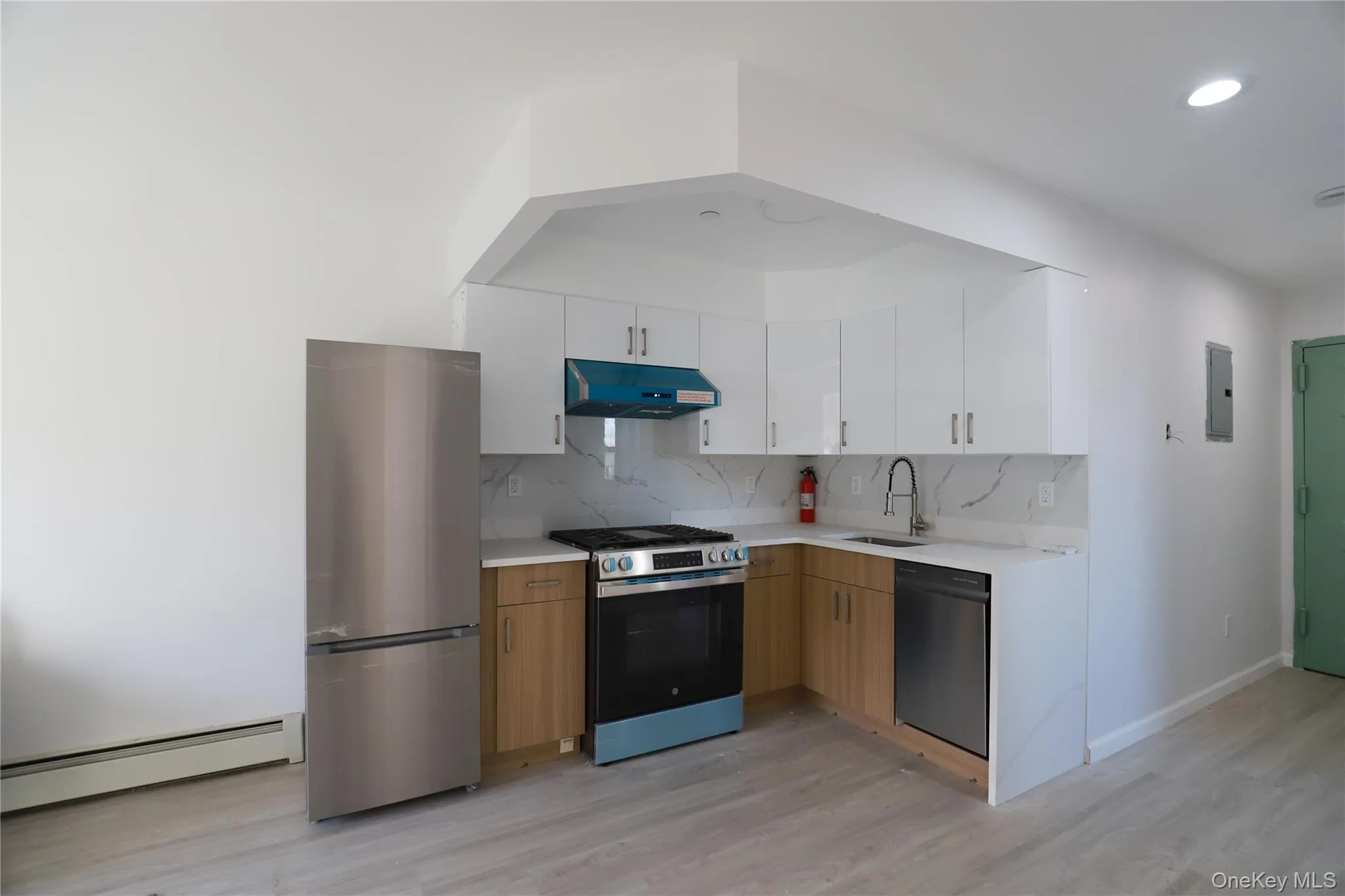 Kitchen featuring appliances with stainless steel finishes, backsplash, a baseboard heating unit, white cabinets, and light wood-type flooring Kitchen featuring appliances with stainless steel finishes, backsplash, a baseboard heating unit, white cabinets, and light wood-type flooring