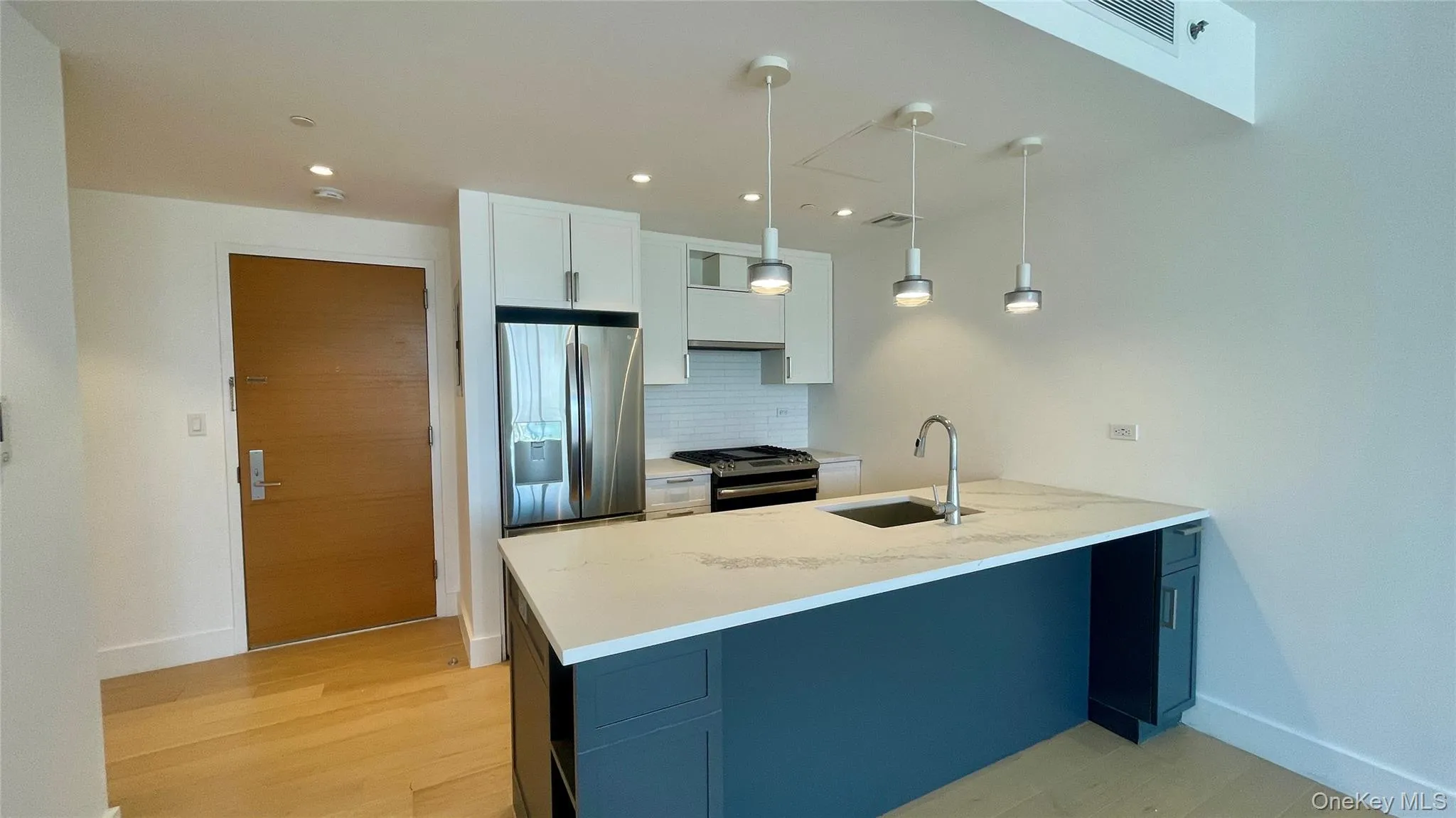 Kitchen with light stone countertops, stainless steel appliances, decorative light fixtures, white cabinets, and backsplash Kitchen with light stone countertops, stainless steel appliances, decorative light fixtures, white cabinets, and backsplash